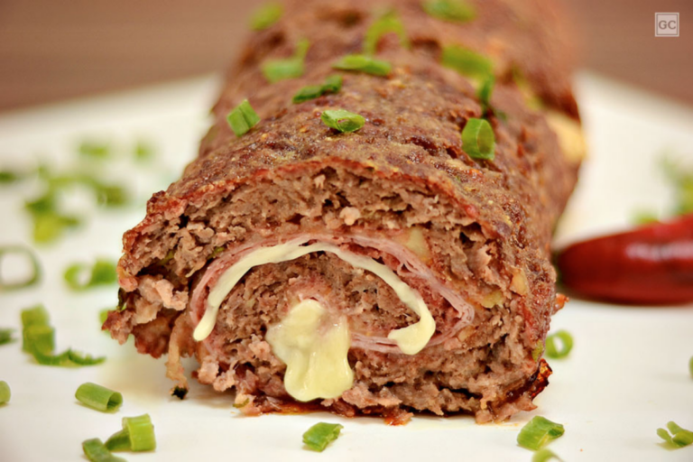 Rocambole de carne recheado, dourado e suculento, servido em uma tábua de madeira com acompanhamentos